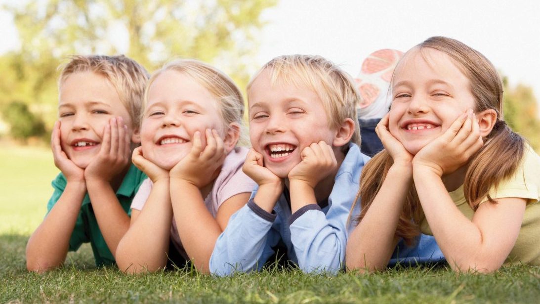 Four smiling 7 year old kids lying on their stomachs with their hands supporting their chins
